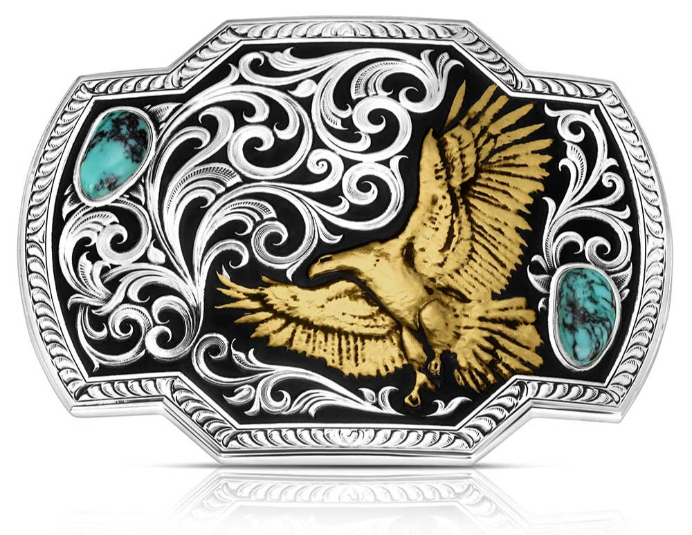 front. Take flight with the Tail Wind belt buckle! Featuring a black backdrop, a golden eagle soars through detailed silver filigree that mimics swirling winds. Crafted Turquoise stones add a pop of color in opposite corners of this rope-edged, rectangle buckle. Measuring about 4.25" wide by 3.25" tall, it fits belts up to 1.5" wide. Snag one at our Smyrna, TN shop—just a quick drive from downtown Nashville! Made by Montana Silversmith.