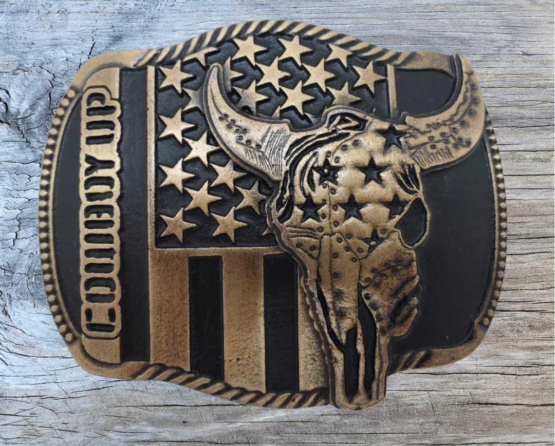 The "Braxton" Belt Buckle is a brass colored oval featuring a Buffalo Skull and a Patriotic USA flag, representing the well-known Rodeo term, "COWBOY UP." It is designed to fit a Standard 1.5 belt and measures approximately 4" x 3". Come visit our shop just outside Nashville in Smyrna, TN to get yours today!
