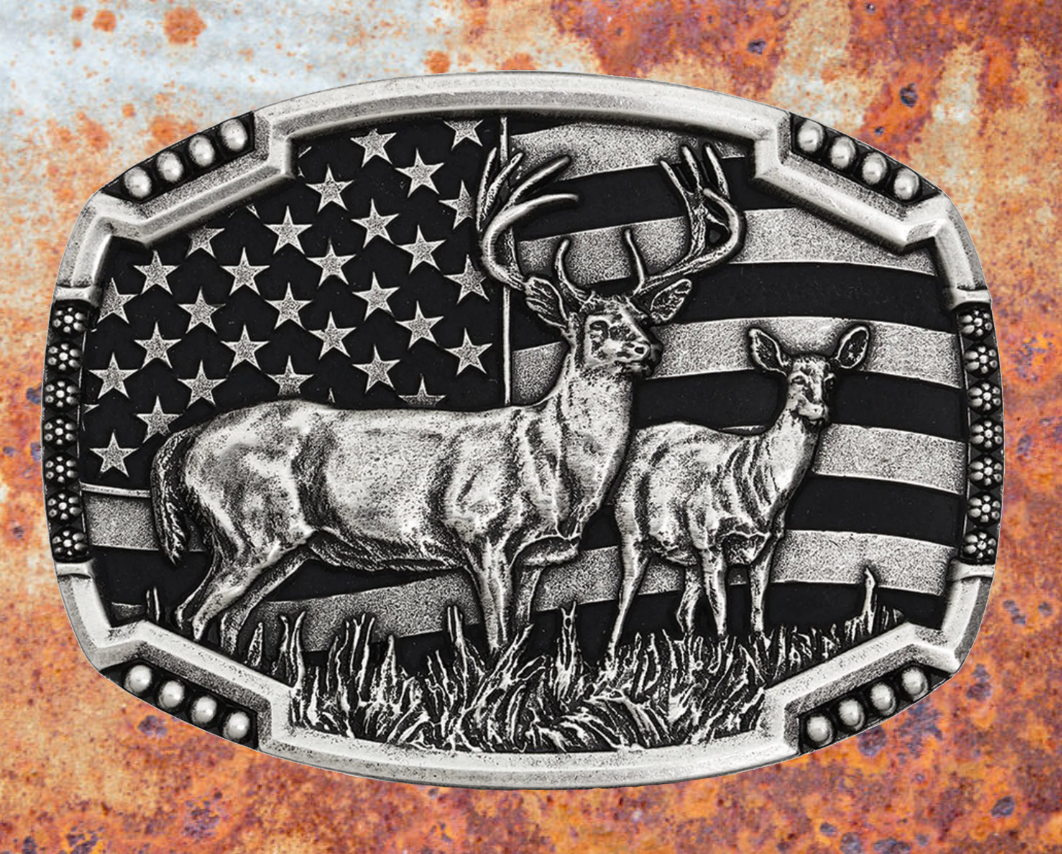 An antiqued silver tone cast buckle with a male and female pair of deer figures standing at attention in the midst of a grassy field. The stars-n-stripes serve as a patriotic backdrop to the animals. The buckle is finished with a smooth wire notched edge with the notches filled with beads. Standard 1.5 inch belt swivel. Available at our shop just outside Nashville in Smyrna, TN. Dimensions: Width 4.00" Height 3.00" Length 0.75"