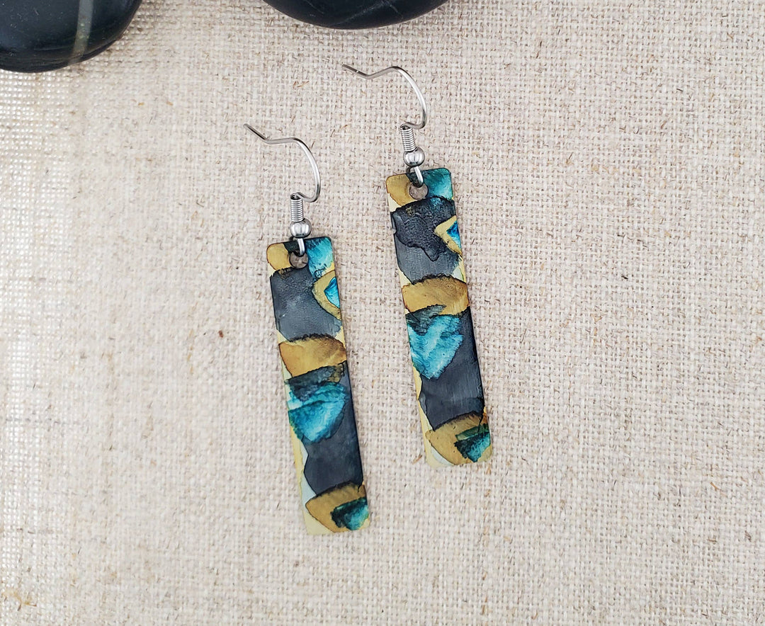 -The stainless steel earring blanks are hand painted with alcohol ink. -They are sealed to keep the finish. -The ear wires are stainless steel. -They measure 2 1/4" in length and 3/8" in width. -Medium weight -THE PHOTO IS AN EXAMPLE OF WHAT YOU WOULD RECEIVE. Each pair is one of a kind. Stocked at our Smyrna, TN shop down I-24 from downtown.