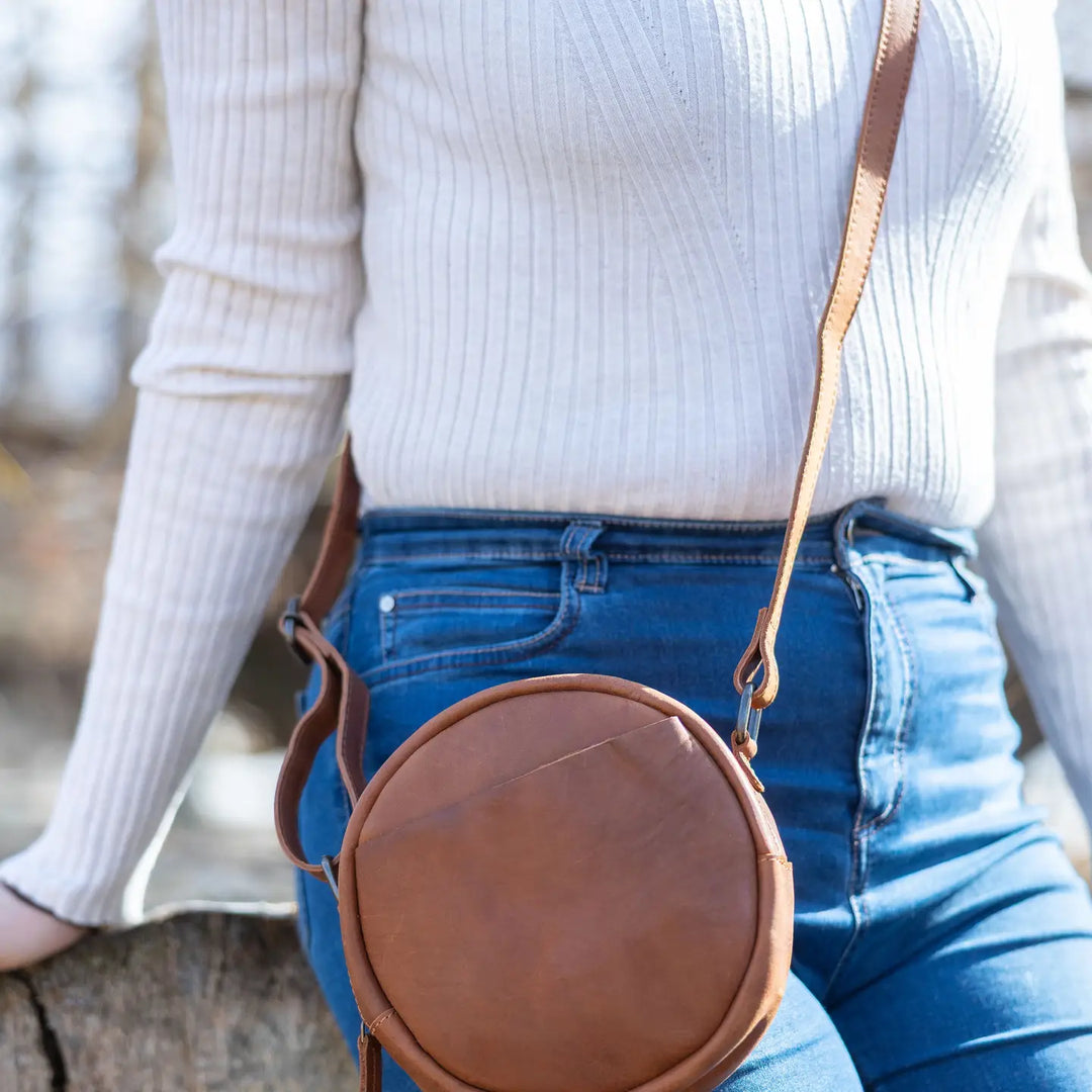 The Greta is a mini round crossbody bag crafted from vegetable-tanned Firenze Antiqua leather. This unlined crossbody features an adjustable strap for perfect fit. The smart key snap attached to the lace ensures effortless access to your essentials, adding a touch of convenience to this elegant accessory. Round everyone up and come see it for yourself at our Smyrna, TN store not far from Murfreesboro.