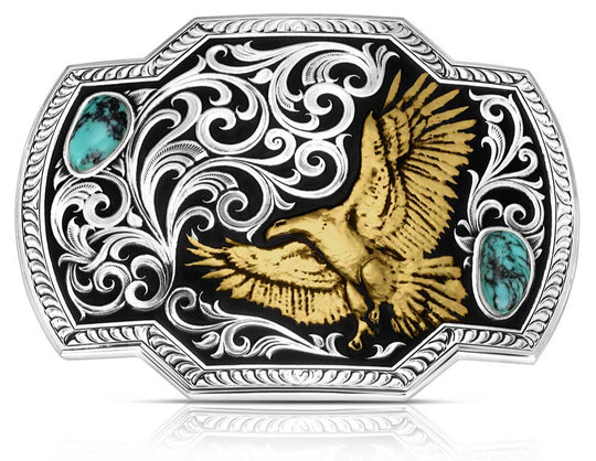 front. Take flight with the Tail Wind belt buckle! Featuring a black backdrop, a golden eagle soars through detailed silver filigree that mimics swirling winds. Crafted Turquoise stones add a pop of color in opposite corners of this rope-edged, rectangle buckle. Measuring about 4.25" wide by 3.25" tall, it fits belts up to 1.5" wide. Snag one at our Smyrna, TN shop—just a quick drive from downtown Nashville! Made by Montana Silversmith.