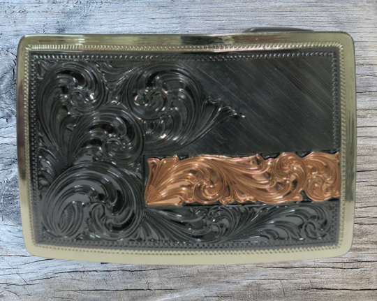 The Illusive is an attractive small, low-profile buckle engraved with a western scroll and diagonal lines. Crafted using a German Silver base, the border is a silver color, while the background is a gunmetal black, accented with a rectangular copper strip running through 2/3rds of the lower half of the buckle. Available in our Smyrna, TN shop, a short distance from Nashville.&amp;nbsp;

Dimensions: Width 3”, Height 2”

Standard 1.5” Swivel