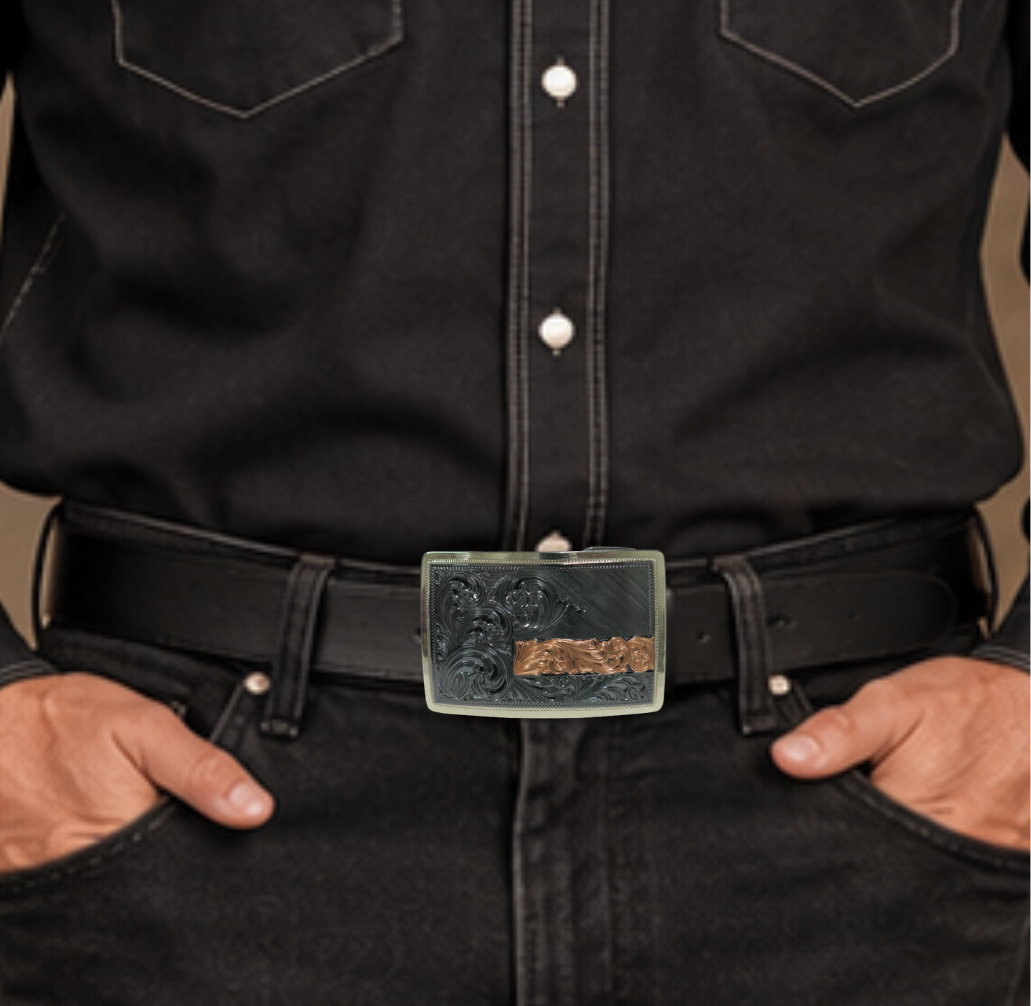 The Illusive is an attractive small, low-profile buckle engraved with a western scroll and diagonal lines. Crafted using a German Silver base, the border is a silver color, while the background is a gunmetal black, accented with a rectangular copper strip running through 2/3rds of the lower half of the buckle. Available in our Smyrna, TN shop, a short distance from Nashville.&amp;nbsp;

Dimensions: Width 3”, Height 2”

Standard 1.5” Swivel