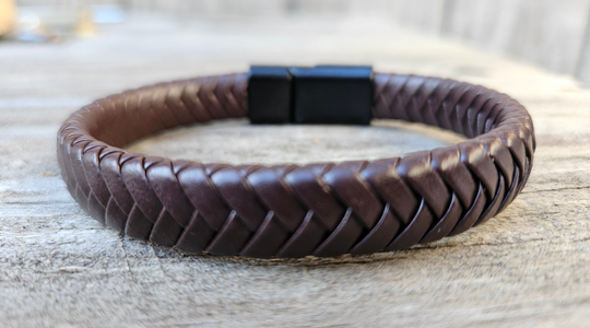 Brown braided leather bracelet with a black magnetic clasp displayed on a wooden surface