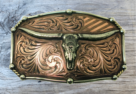 The Chief Longhorn buckle  These buckles are made from German Silver (nickel and brass alloy) or iron metal base. Some buckles have motifs made of copper, iron or brass and some are adorned with synthetic stones. These are all handcrafted. Each piece is punched, cut, soldered, engraved, polished and painted by our talented metal workers.  Available in our Smyrna TN shop. Width 4.5” Height 3”
Fits Standard 1.5” belts