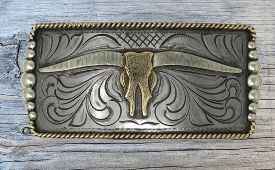 One of our more unique buckles, it has a rectangle shape with a Western scroll design, and a beaded rope edge framing a Longhorn steer. This buckle is made from German Silver (nickel and brass alloy) or iron metal base. Some buckles have motifs made of copper, iron or brass and some are adorned with synthetic stones. Buckle size is Width 5” Height 2” and is available in our Smyrna, TN shop.