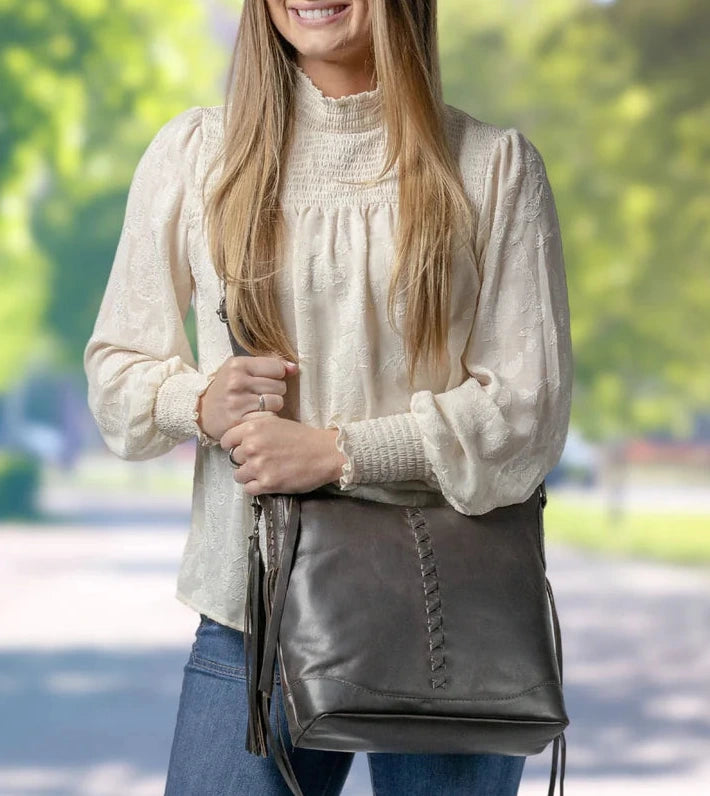 The Blake Scooped Leather Crossbody is crafted from premium full-grain leather, each piece showcasing its own natural variations in grain and shading. Intricate leather crisscross stitching adorns the front and sides, complemented by decorative long tassels for added charm. A large open pocket for your cell phone, and a leather key strap. A zippered pocket on the back adds more room for your essentials. Part of our Carry Conceal Handbags in our Smyrna, TN shop.