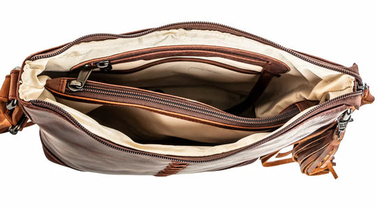 The Blake Scooped Leather Crossbody is crafted from premium full-grain leather, each piece showcasing its own natural variations in grain and shading. Intricate leather crisscross stitching adorns the front and sides, complemented by decorative long tassels for added charm. A large open pocket for your cell phone, and a leather key strap. A zippered pocket on the back adds more room for your essentials. Part of our Carry Conceal Handbags in our Smyrna, TN shop.