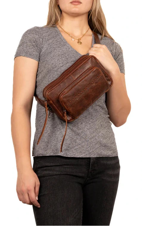 The Laney Belt Bag, crafted from buffalo leather, showcases a decorative scalloped design. This versatile accessory can be worn around the waist or as a sling, combining style and convenience. The bag is thoughtfully divided into three sections with a main interior, located in the middle compartment, secured with a leather strap with a magnetic snap closure. The concealed carry compartment is discreetly located in the back. Part of our Carry Conceal Handbags at our Smyrna, TN shop.