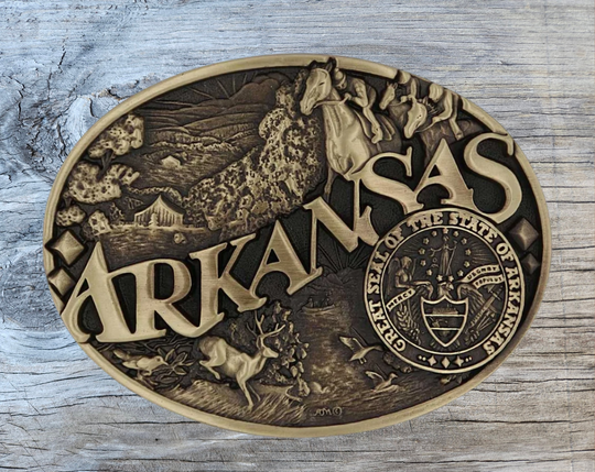 Large lettering spelling out Arkansas stretches boldly across, surrounded by a set of antiqued figures in celebration of Arkansas heritage including horse racing, wildlife, and the state seal. Our cast belt buckles are acid washed to add the dark antiqued patina and hand buffed to bring out the highlights and details. Standard 1.5 inch belt swivel.
&amp;nbsp;Get yours at our local Smyrna ,TN shop.
Width 3.75 Height 2.75
Materials Brass plate over a solid cast metal alloy base