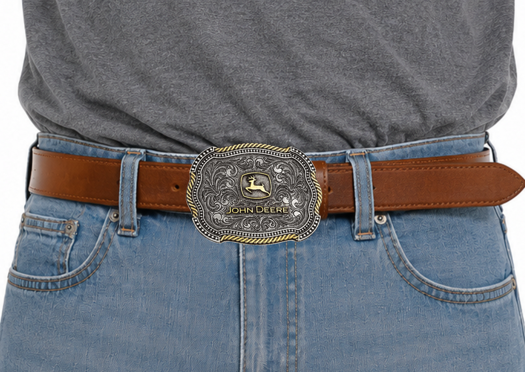 An officially licensed John Deere® two tone cast in antiqued silver and gold tones with a softly scalloped edge. The classic gold toned John Deere logo sits in the center of the buckle surrounded by antiqued silver toned filigree design. The edges of the filigree are lined by a scalloped shaped edging of silver toned microbeads with the outer edge a combination of sections gold toned rope and silver toned microbeads alternating their way around the edge. Standard 1.5 inch belt swivel. In stock at our Smyrna
