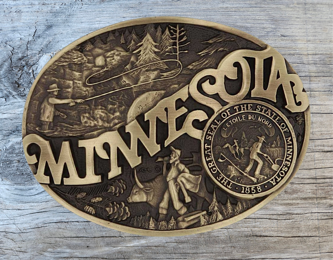 Celebrate Minnesota State with this buckle highlighting fly fishing, the golden era of logging, and the great state seal! Brass plate over a solid cast metal alloy is antiqued and buffed to highlight the details.

Fits 1 1/2" belts and is approx. 3" tall x 4" across. Available at our shop just outside Nashville in Smyrna, TN. Made by Montana Silversmiths.
