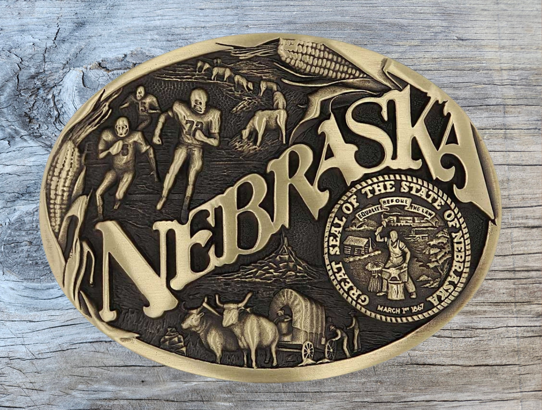 Celebrate Nebraska State with this oval buckle highlighting football, corn, pioneers, and the great state seal! Brass plate over a solid cast metal alloy is antiqued and buffed to highlight the details.

Fits 1 1/2" belts and is approx. 3" tall x 4" across. Available at our shop just outside Nashville in Smyrna, TN. Made by Montana Silversmiths.