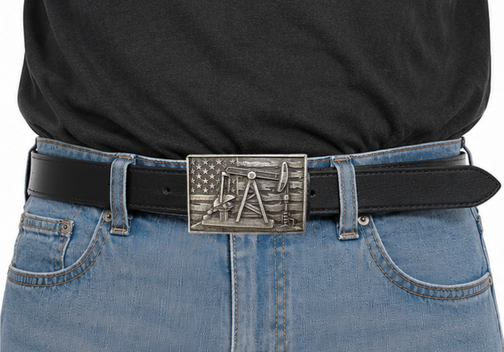 The Pump Jack Buckle features a rectangular design showcasing an oil rig pump jack against a weathered American flag backdrop. Crafted from zinc and iron with a dark antique silver finish, it measures about 2 1/2" by 3 3/4" and fits a standard 1 1/2" belt. Grab yours online or visit our Smyrna, TN shop near Nashville to add some rugged charm to your look!