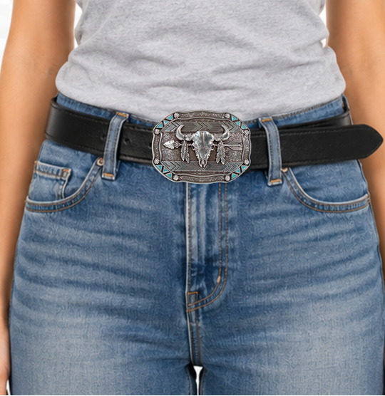 This belt buckle takes inspiration from the Lakota people, known for their buffalo hunting practices. It features an oval shape with small turquoise triangles and berry shapes along the border. In antique silver, it showcases a buffalo skull, feathers, and an arrow in the center. Measuring approximately 3" tall by 4" wide, it can fit belts up to 1 1/2" wide. You can find it in our retail shop in Smyrna, TN, near Nashville, or on our online store.
