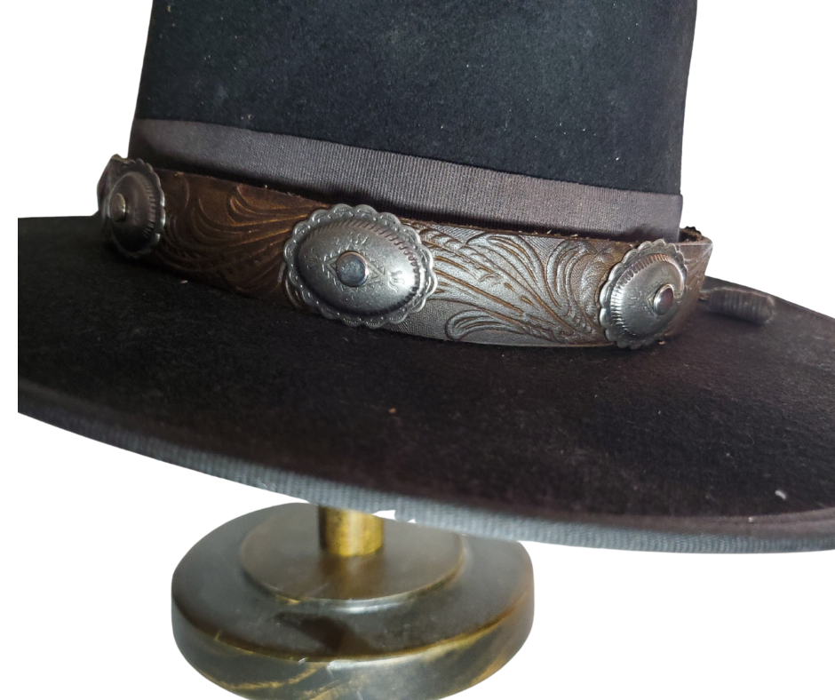 A classic Western Styled pattern with a Southwest Antique nickel concho completes our <b><i>Rustler Hand Stained</i></b> leather hatband. Band is 1" wide will fit up to size 7 1/2 hat. Matches our Rustler Belt. Fit's most any hat with adjustable bead and leather 1/8" string. Will fit most WESTERN crowned hats. Made in our Smyrna, TN. shop a short drive from downtown Nashville, TN.