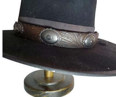 A classic Western Styled pattern with a Southwest Antique nickel concho completes our <b><i>Rustler Hand Stained</i></b> leather hatband. Band is 1" wide will fit up to size 7 1/2 hat. Matches our Rustler Belt. Fit's most any hat with adjustable bead and leather 1/8" string. Will fit most WESTERN crowned hats. Made in our Smyrna, TN. shop a short drive from downtown Nashville, TN.