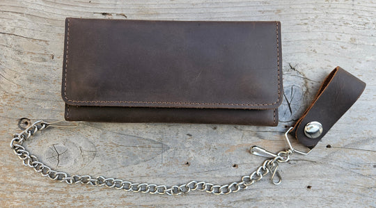 The Road Dog Tri-fold Biker Wallet is a lightweight leather thin profile chain wallet with a basic chrome plated chain that is detachable. Snap-button closure, 5 credit card slots, 1 clear ID window, 1 zippered coin pocket, 3 full-length storage pockets for cash, receipts, or additional cards. Offered in a black and brown. Closed Size: 7" L × 3.5" H. Available at our Smyrna, TN shop, near Nashville.
