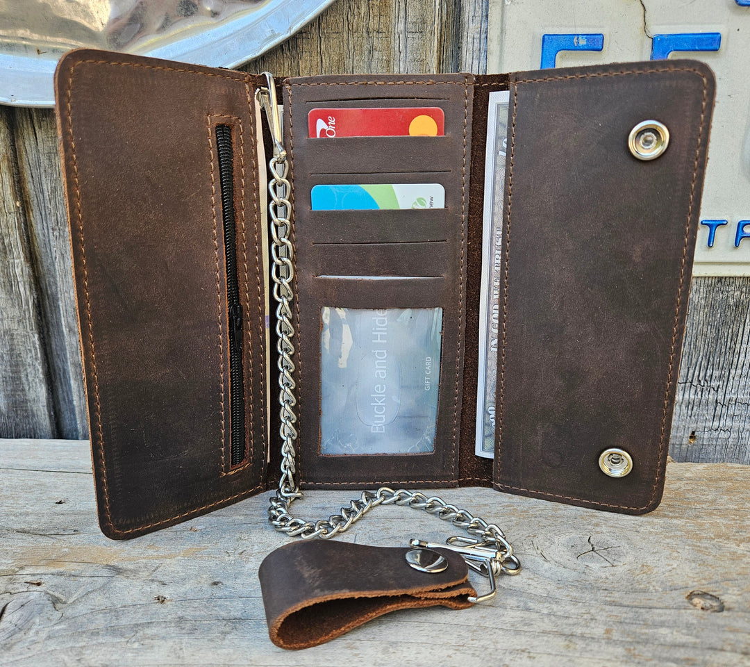The Road Dog Tri-fold Biker Wallet is a lightweight leather thin profile chain wallet with a basic chrome plated chain that is detachable. Snap-button closure, 5 credit card slots, 1 clear ID window, 1 zippered coin pocket, 3 full-length storage pockets for cash, receipts, or additional cards. Offered in a black and brown. Closed Size: 7" L × 3.5" H. Available at our Smyrna, TN shop, near Nashville.