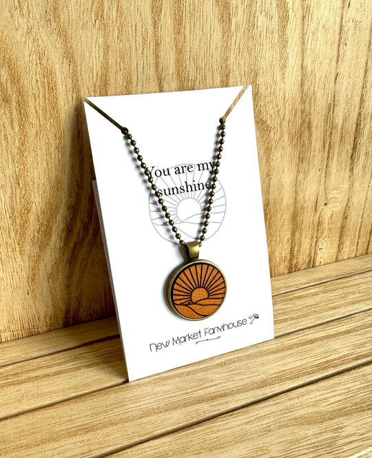 Farmhouse Leather Necklaces, Stocked at our Smyrna, TN shop. Currently offered in a Cross, Butterfly, and a Sunrise scene.

Each Necklace is made from laser engraved veg tan leather, set in an Antique Bronze 1" metal bezel and dangles from a matching 20" ball chain. Dimensions: 5 x 4 x 0.5 in.