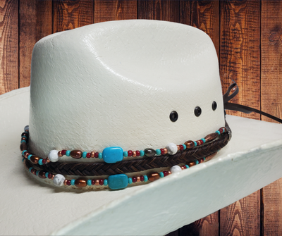 This trendy hatband features a seven strand braid made of genuine horse hair, adorned with coppery metal beads, white and turquoise howlite, and freshwater pearls. It is completed with our signature sunburst conchos, leather tassels, and a horse hair knot for secure fit. Designed to fit most hats, it is available at our Smyrna, Tn shop. Every piece is carefully handcrafted in Montana using horse hair from various sources including Argentina, Mongolia, and Canada.