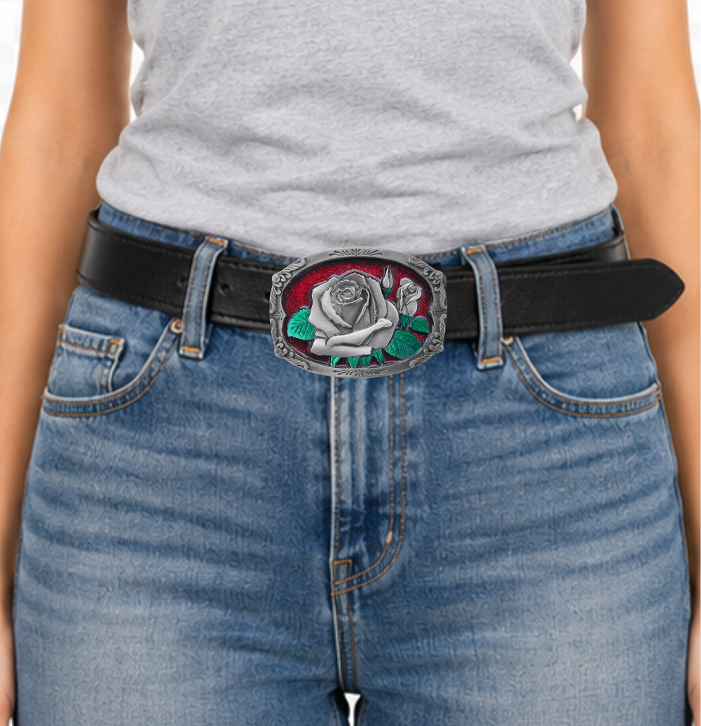 The "Rose Bud" belt buckle showcases a blooming rosebud highlighted with red and green enamel inlays, framed by a delicate filigree border on a semi-rectangular design. Proudly made in the USA, this solid metal cast buckle measures 2 7/8" by 2 1/16". Crafted from lead-free zinc aluminum and coated with non-toxic epoxy enamel, it fits belts up to 1 3/4" wide. Find this charming buckle in our Smyrna, TN shop just outside Nashville.