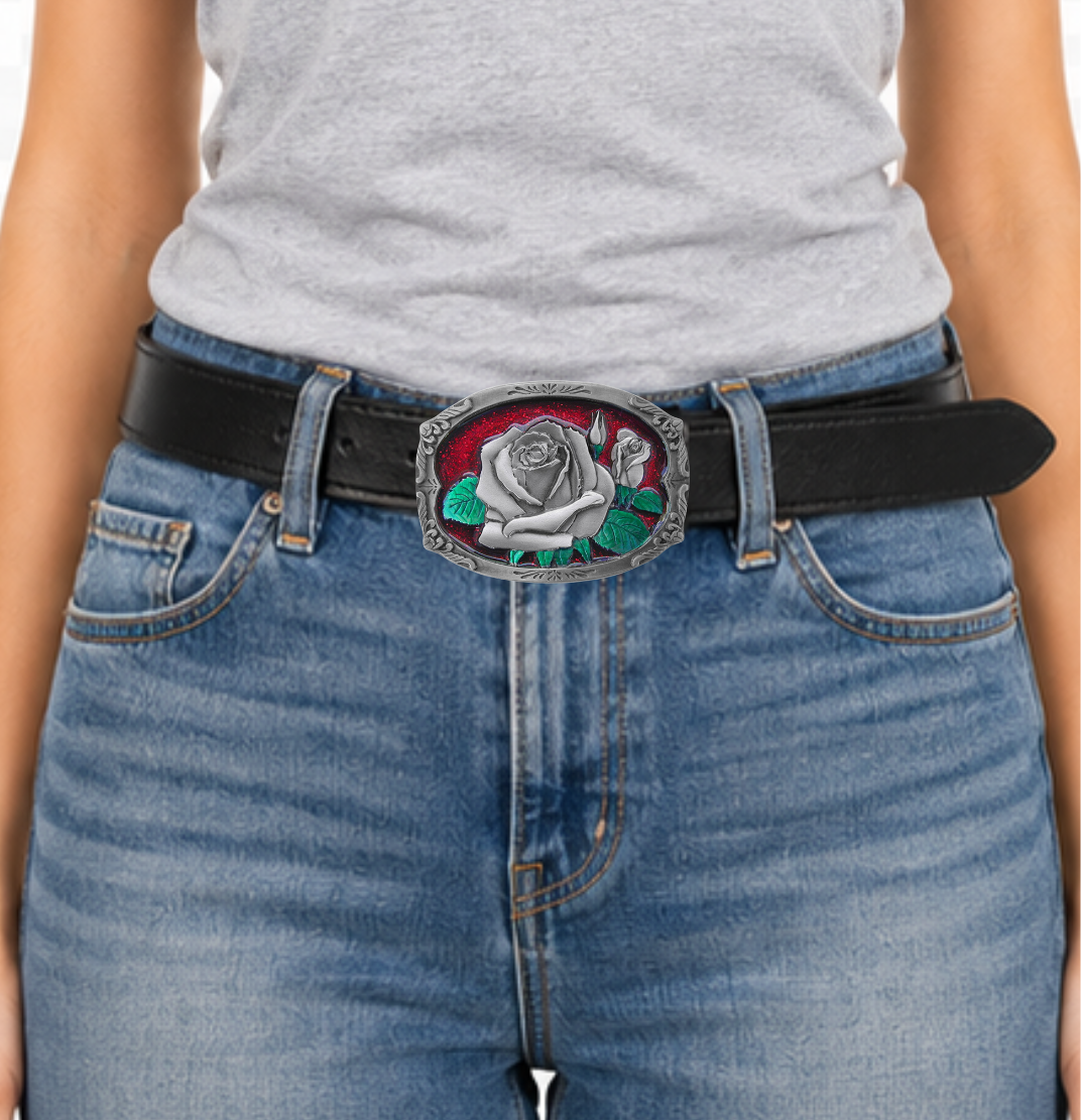 The "Rose Bud" belt buckle showcases a blooming rosebud highlighted with red and green enamel inlays, framed by a delicate filigree border on a semi-rectangular design. Proudly made in the USA, this solid metal cast buckle measures 2 7/8" by 2 1/16". Crafted from lead-free zinc aluminum and coated with non-toxic epoxy enamel, it fits belts up to 1 3/4" wide. Find this charming buckle in our Smyrna, TN shop just outside Nashville.