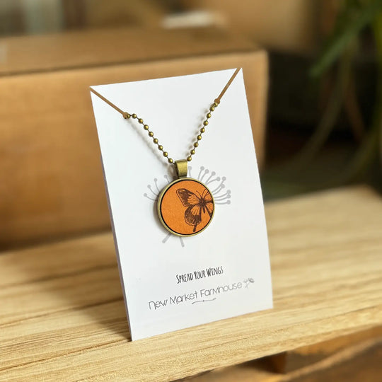 Farmhouse Leather Necklaces, Stocked at our Smyrna, TN shop. Currently offered in a Cross, Butterfly, and a Sunrise scene.

Each Necklace is made from laser engraved veg tan leather, set in an Antique Bronze 1" metal bezel and dangles from a matching 20" ball chain. Dimensions: 5 x 4 x 0.5 in.