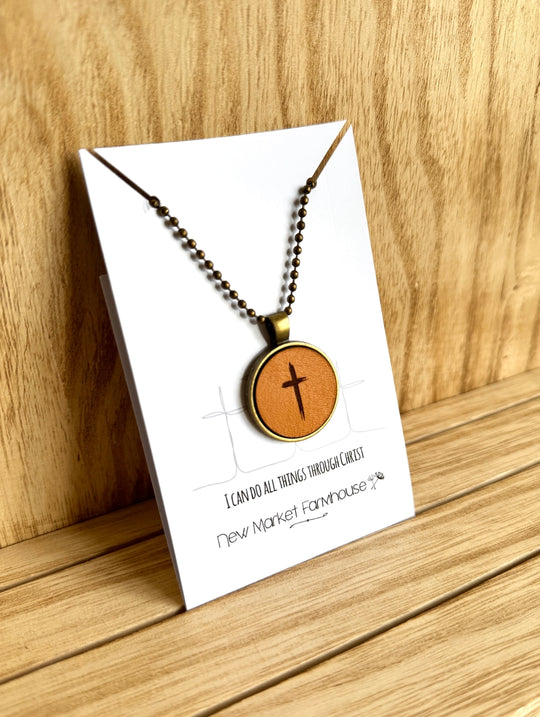 Farmhouse Leather Necklaces, Stocked at our Smyrna, TN shop. Currently offered in a Cross, Butterfly, and a Sunrise scene.

Each Necklace is made from laser engraved veg tan leather, set in an Antique Bronze 1" metal bezel and dangles from a matching 20" ball chain. Dimensions: 5 x 4 x 0.5 in.