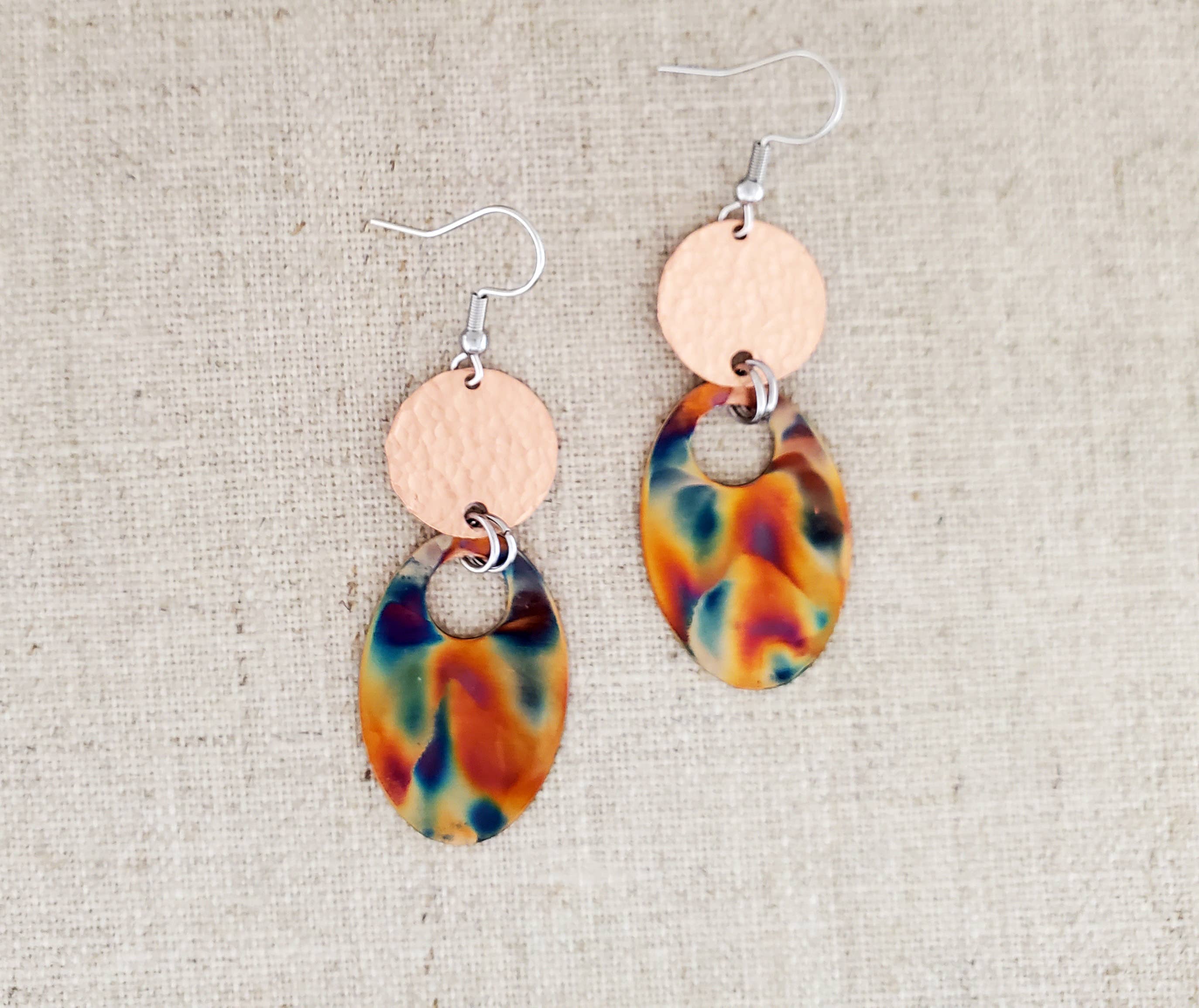 -Hand cut and finished copper blanks that are then flame painted with a torch. The connector piece is hammered for texture. -Sealed to keep the finish -Ear wires are stainless steel. -2 1/2" in length and 3/8" in width -Medium weight -Each pair of earrings will look similar to the above pictured pair, but will vary slightly in color and pattern due to dealing with torch. Stocked at our Smyrna, TN shop down I-24 from downtown.
