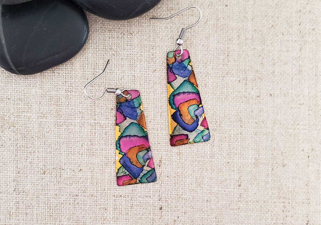 -The earrings are hand cut and finished copper blanks that are then hand painted with alcohol ink. -They are sealed to keep the finish. -The ear wires are stainless steel. -They measure 2" in length and 5/8" in width. -Light weight -THE PHOTO IS AN EXAMPLE OF WHAT YOU WOULD RECEIVE. Each pair is one of a kind. Stocked at our Smyrna, TN shop down I-24 from downtown.