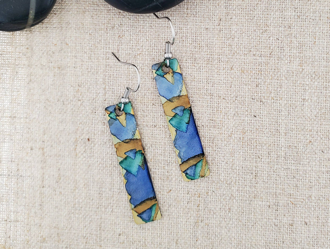 -The stainless steel earring blanks are hand painted with alcohol ink. -They are sealed to keep the finish. -The ear wires are stainless steel. -They measure 2 1/4" in length and 3/8" in width. -Medium weight -THE PHOTO IS AN EXAMPLE OF WHAT YOU WOULD RECEIVE. Each pair is one of a kind. Stocked at our Smyrna, TN shop down I-24 from downtown.