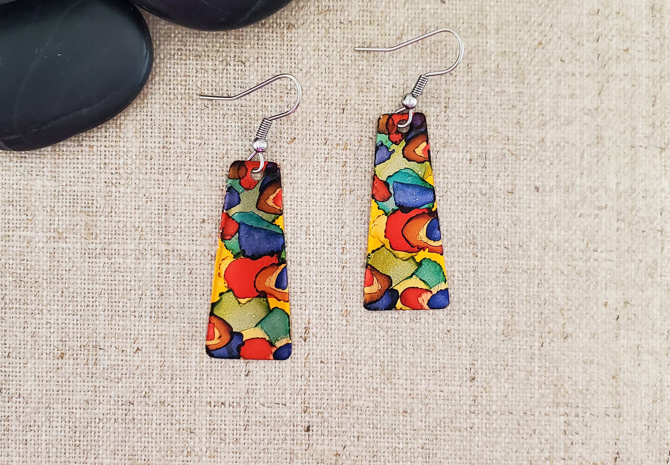-The earrings are hand cut and finished copper blanks that are then hand painted with alcohol ink. -They are sealed to keep the finish. -The ear wires are stainless steel. -They measure 2" in length and 5/8" in width. -Light weight -THE PHOTO IS AN EXAMPLE OF WHAT YOU WOULD RECEIVE. Each pair is one of a kind. Stocked at our Smyrna, TN shop down I-24 from downtown.