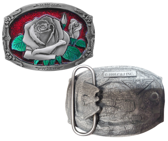 The "Rose Bud" belt buckle showcases a blooming rosebud highlighted with red and green enamel inlays, framed by a delicate filigree border on a semi-rectangular design. Proudly made in the USA, this solid metal cast buckle measures 2 7/8" by 2 1/16". Crafted from lead-free zinc aluminum and coated with non-toxic epoxy enamel, it fits belts up to 1 3/4" wide. Find this charming buckle in our Smyrna, TN shop just outside Nashville.