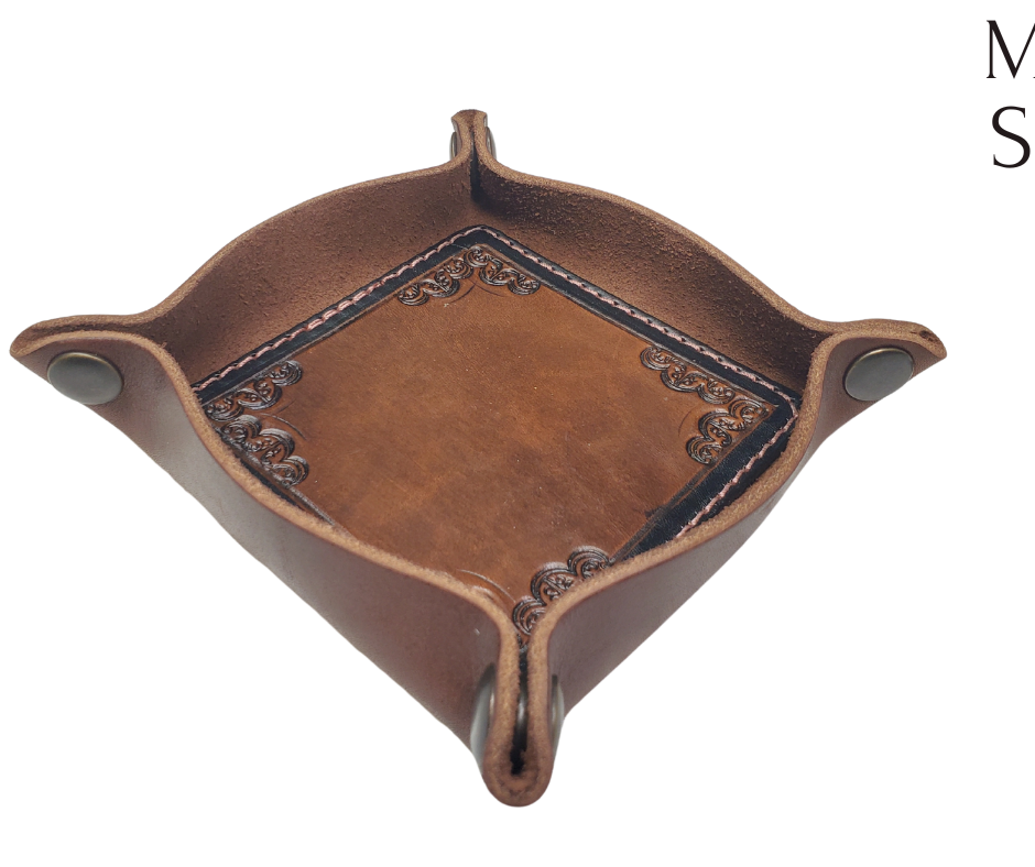 The Franklin is a little different than our other trays because of the Hand Stamped and stained inside layer. Outer layer is a Bison brown color with the inside layer being stitched in. The corners are held together with heavy line 24 Antique Brass colored snaps, for laying flat for travel, a place for placing keys, wallet, coins, etc. Made in our shop just outside Nashville in Smyrna, TN.