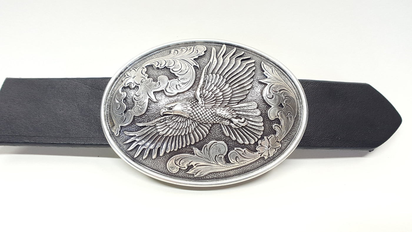 Nocona Eagle Buckle, Nocona Western buckle  Smooth edge oval shaped buckle centered with a flying eagle and floral scroll on either side of it. Measures: 3" tall X 4" wide Available online and in our shop in Smyrna, TN, just outside of Nashville