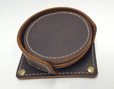 Handmade leather drink coasters with holder.  Made just outside Nashville in Smyrna, TN. Coasters come in set of 6 round 3 1/2" diameter pieces either with matching stitching or contrast stitching around the edges.  They are available in distressed brown. Color variations may occur within sets depending on hides available. Corral square piece of leather with rounded edges and rounded retaining edge approx. 1' tall riveted in place to provide secure placement of coasters when not in use.