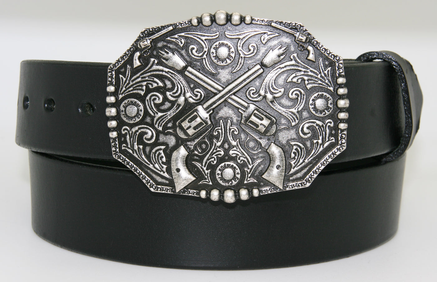 Crossed pistols buckle pictured on black belt-This antique silver colored buckle by AndWest features a pair of crossed pistols centered on the oval shaped buckle with flattened sides. It also features 50 caliber shell end replicas within the Western scroll background design.  Fits belts up to 1 1/2" wide, dimensions are 3" tall by 4" wide.  Available in our online store as well as the retail shop in Smyrna, TN, just outside of Nashville.  This buckle is made in Mexico.