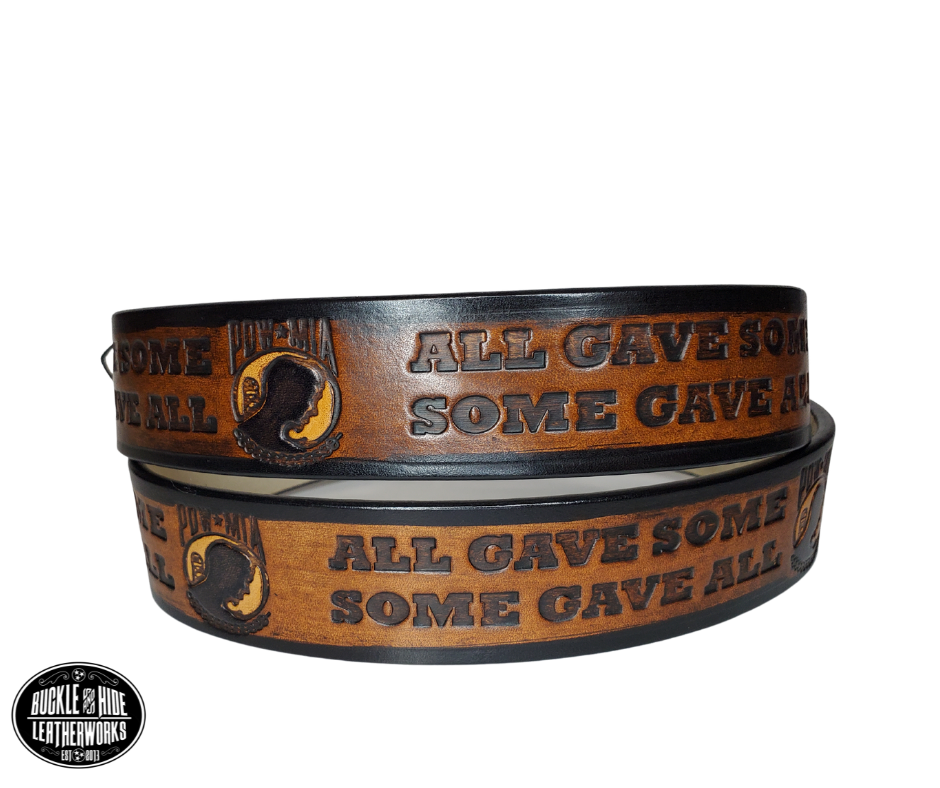 "The Veteran" is a handmade real leather belt made from a single strip of cowhide shoulder leather that is 8-10 oz. or approx. 1/8" thick. It has hand burnished (smoothed) edges and features a POW-MIA emblem along with "SOME GAVE ALL- ALL GAVE SOME pattern down the center. This belt is completely HAND dyed with a multi step finishing technic. The antique nickel plated solid brass buckle is snapped in place with heavy snaps.  This belt is made just outside Nashville in Smyrna, TN.