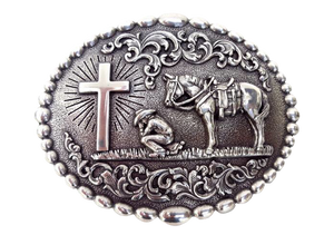 Nocona buckle with beaded edge. Cowboy kneeling at Cross with his trusted horse behind him. A raised floral design perfectly complements this reverent design. Measures 3-1/8" tall by 4" wide  Available online and in our shop in Smyrna, TN, just outside of Nashville