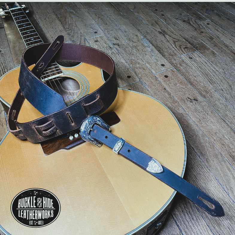You don't get more classic than a handcrafted Distressed leather guitar strap! Featuring a ornate 3 piece western buckle set in the front position of the strap. Each size of buckle set is similar but not the same, so check out pictures. It's made from 1/8" thick drum distressed water buffalo and looks like a vintage "Tele". The main strap is made from a single strip of leather with beveled and .  Choose a 2" or 2 1/2" wide strap with a classic adjustment style.  Made just outside Nashville in Smyrna, TN.