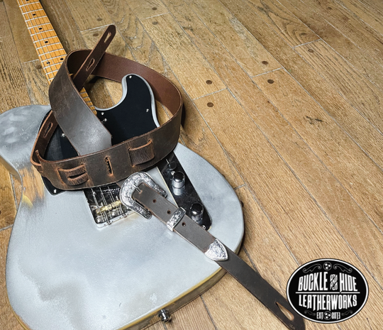 You don't get more classic than a handcrafted Distressed leather guitar strap! Featuring a ornate 3 piece western buckle set in the front position of the strap. Each size of buckle set is similar but not the same, so check out pictures. It's made from 1/8" thick drum distressed water buffalo and looks like a vintage "Tele". The main strap is made from a single strip of leather with beveled and .  Choose a 2" or 2 1/2" wide strap with a classic adjustment style.  Made just outside Nashville in Smyrna, TN.