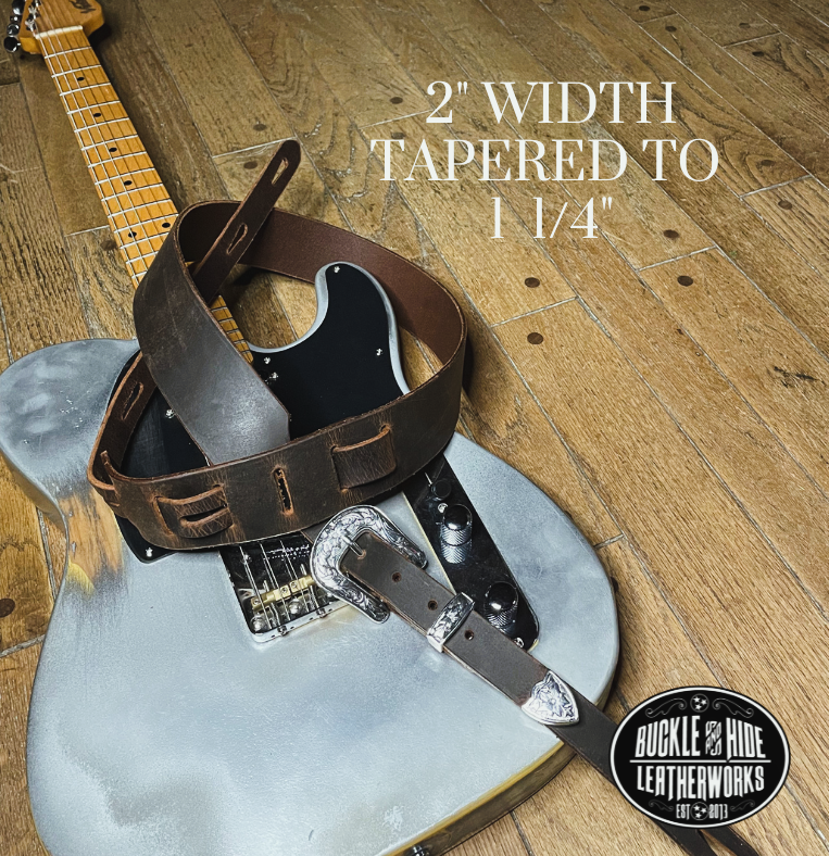 You don't get more classic than a handcrafted Distressed leather guitar strap! Featuring a ornate 3 piece western buckle set in the front position of the strap. Each size of buckle set is similar but not the same, so check out pictures. It's made from 1/8" thick drum distressed water buffalo and looks like a vintage "Tele". The main strap is made from a single strip of leather with beveled and .  Choose a 2" or 2 1/2" wide strap with a classic adjustment style.  Made just outside Nashville in Smyrna, TN.